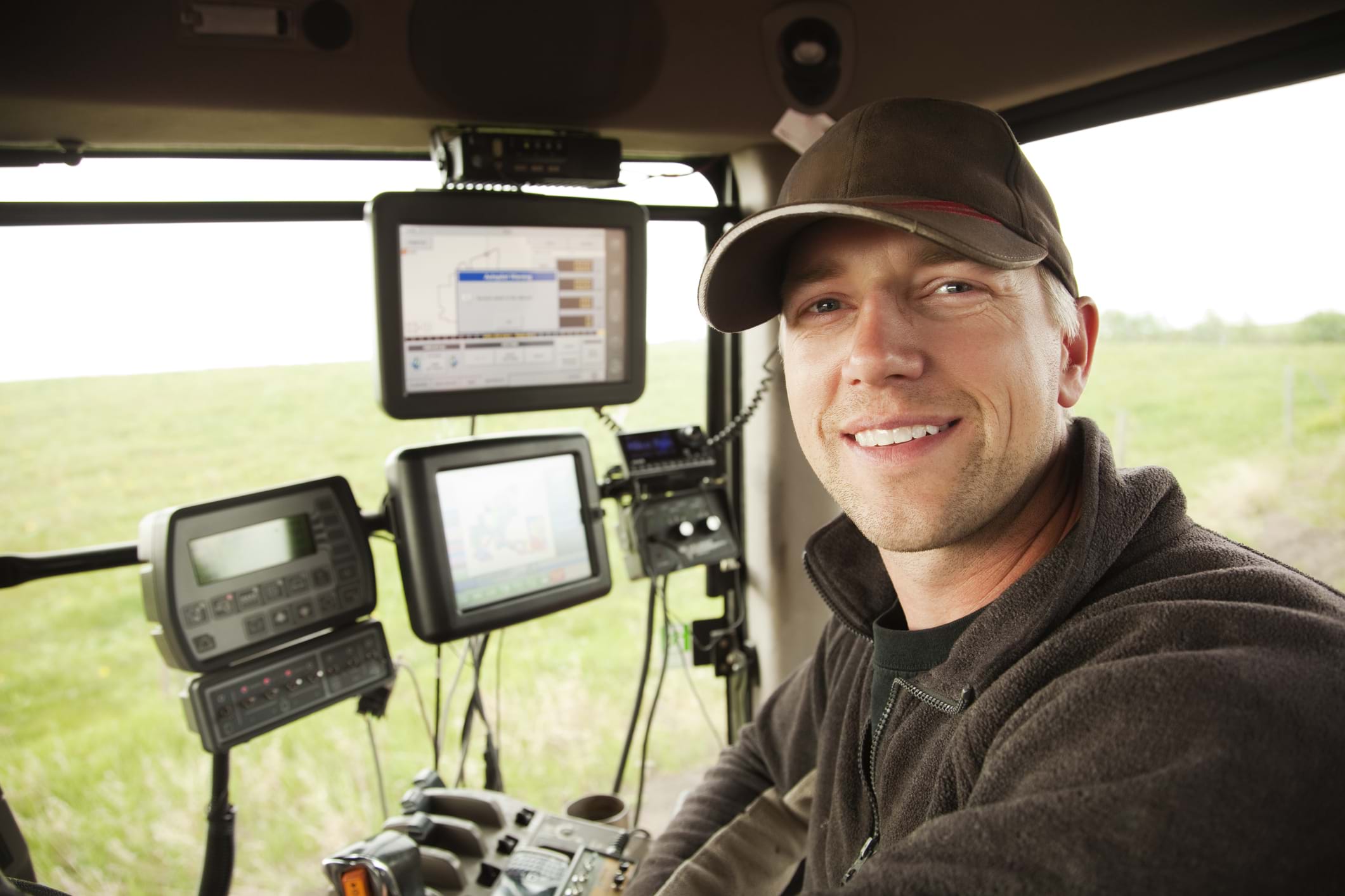 Farm worker sitting in a tractor with cutting-edge technology and monitors, but is the worker a contractor or employee?