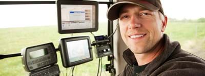 Farm worker sitting in a tractor with cutting-edge technology and monitors, but is the worker a contractor or employee?