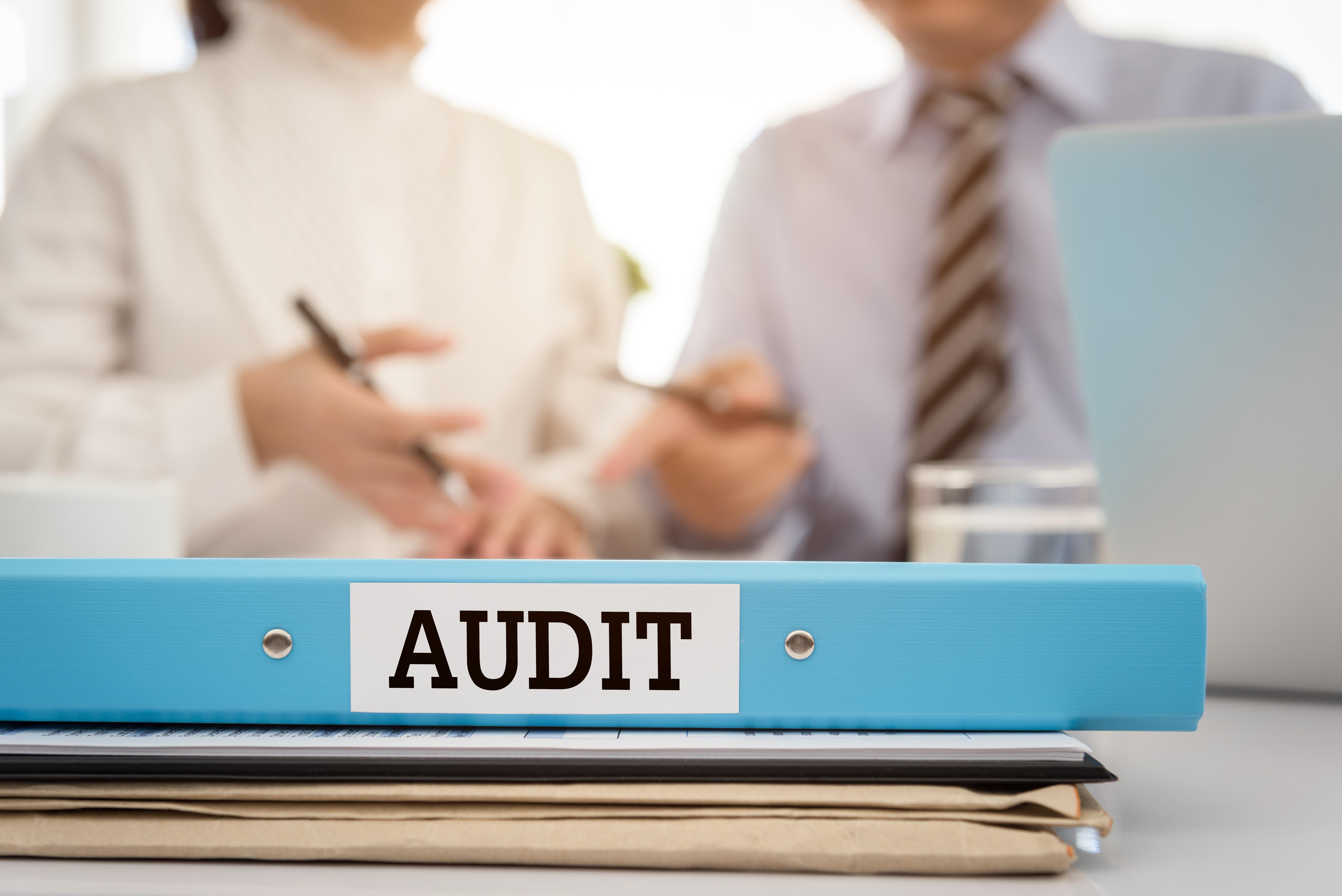 Image of auditing file and paperwork, and two business professionals discussing an audit
