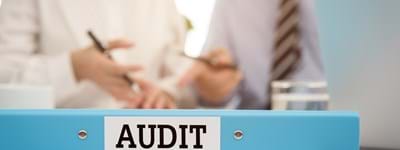 Image of auditing file and paperwork, and two business professionals discussing an audit